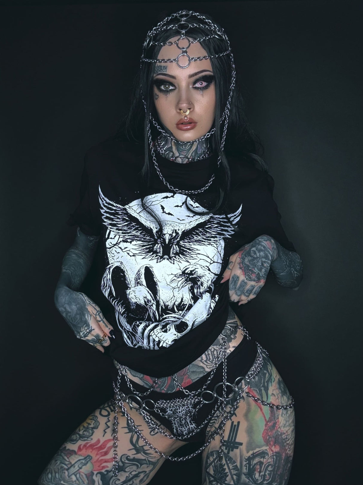 Tätowierte Frau mit Kettenkopfschmuck und grafischem T-Shirt.