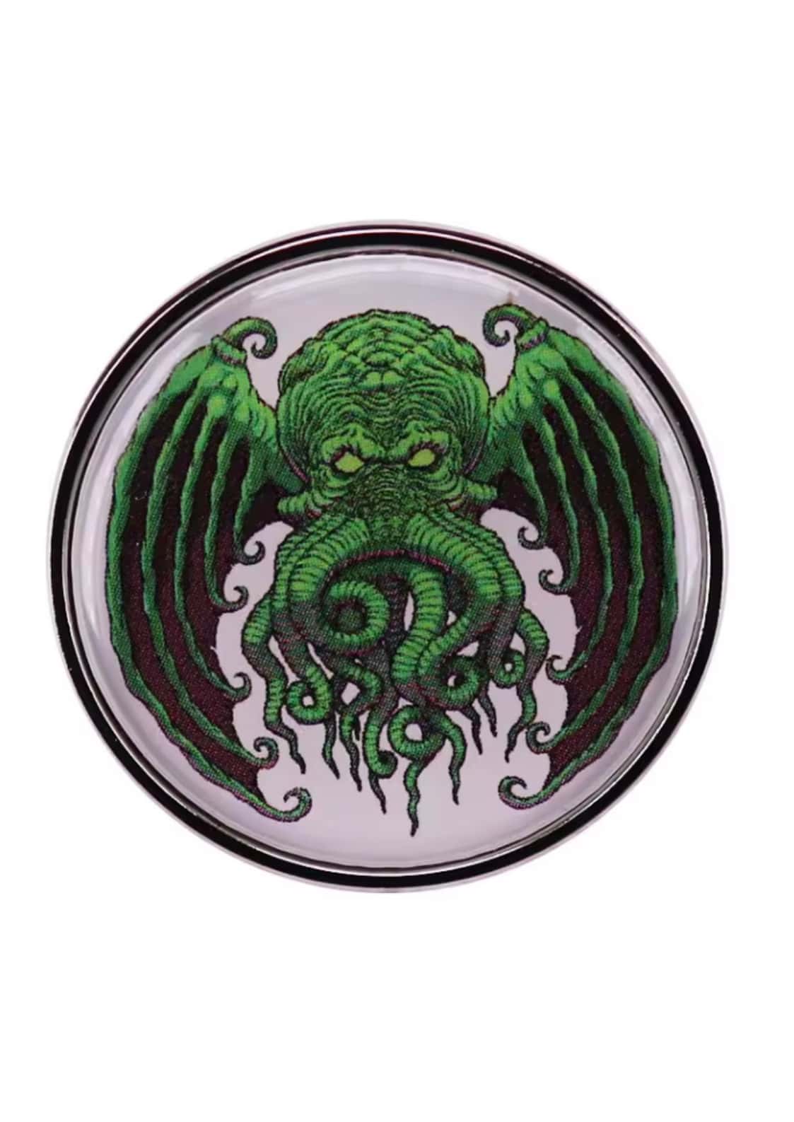 A circular metallic pin featuring a detailed green cthulhu design with gothic tentacles and wings