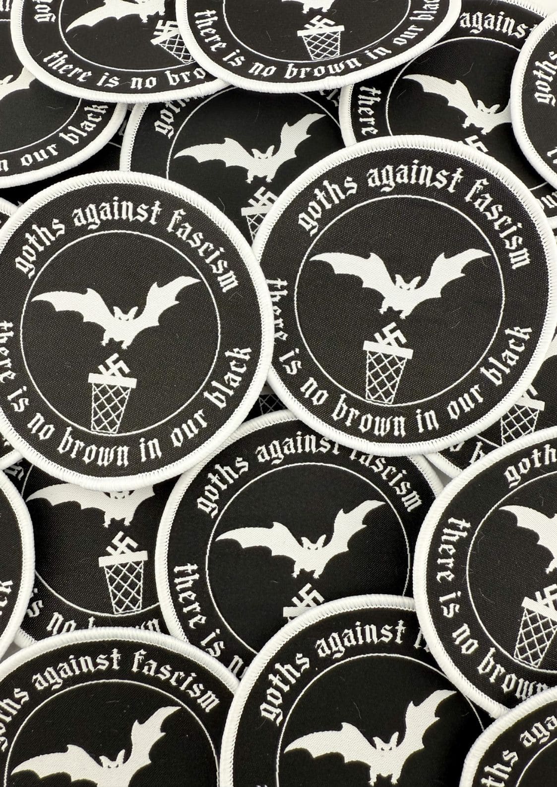 Schwarze runde Flecken mit weiß bestickten Fledermäusen, Swastikas in einem Mülleimer und dem Text ‚Goths gegen Faschismus‘ und ‚in unserem Schwarz gibt es kein Braun.‘