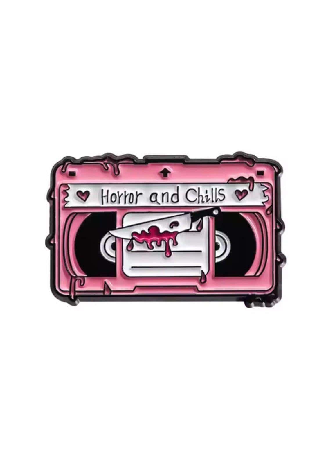 Pink enamel pin in cassette tape shape with horror and chills label and knife through blood red film for gothic dark fashion