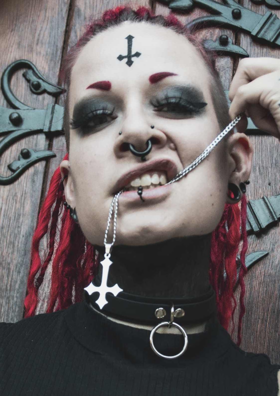 Gothic-Frau mit Piercings und umgekehrtem Kreuzschmuck.