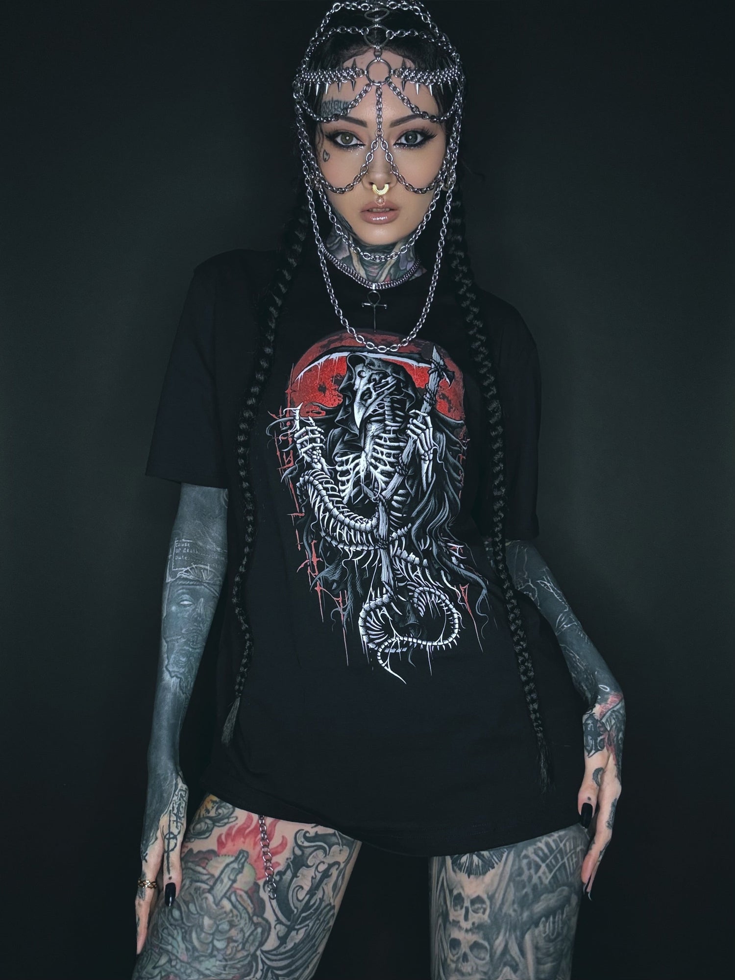 Tätowierte Frau, die einen Kettenkopfschmuck und ein grafisches T-Shirt trägt.