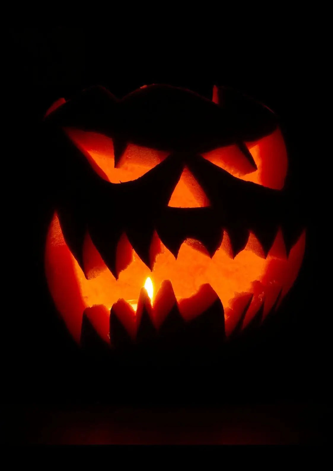 Ein glühender oranger halloween deko jack-o-lantern mit menacing geschnitztem gesicht und warmem kerzenlicht