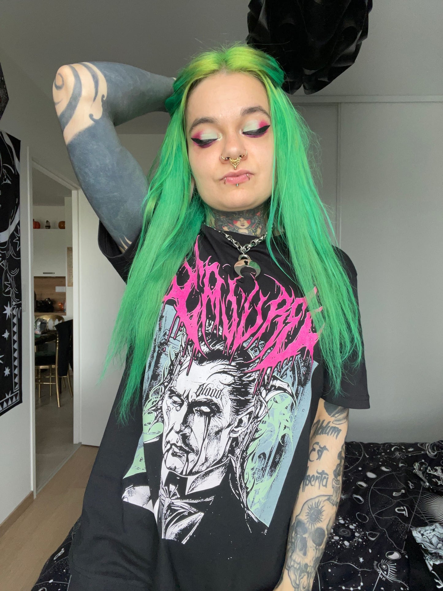 Frau mit grünen Haaren und Tattoos trägt ein grafisches T-Shirt.