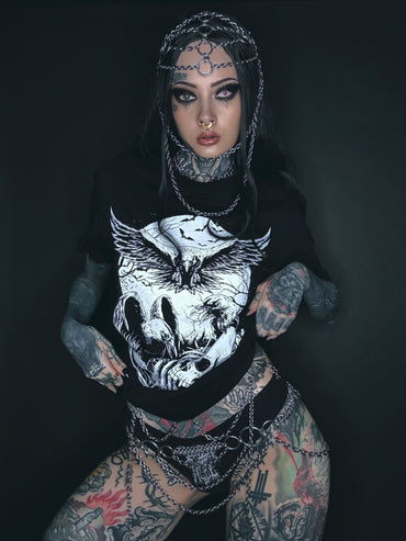 Tätowierte Frau mit Kettenkopfschmuck und grafischem T-Shirt.