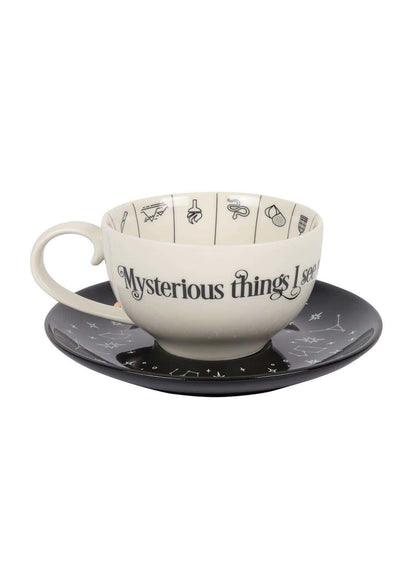 Creamfarbene keramik teetasse mit wahrsage- und astrologischen symbole verziert auf passendem untersetzer