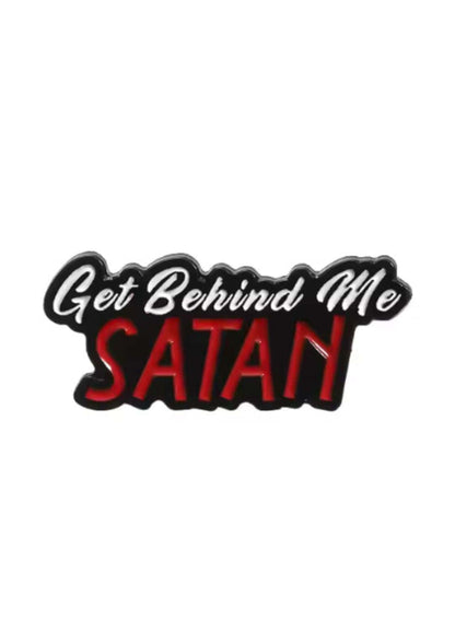 Roter und schwarzer Emaille-Anstecker mit dem Spruch »Weiche mir aus, Satan« in einer fetten, stilisierten Schrift.