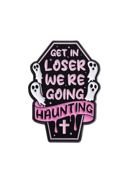 Ein schwarzer, sargförmiger Emaille-Anstecker mit pinker Schrift, die ‘steig ein, Verlierer, wir gehen spuken’ sagt, und weißen Geisterfiguren darum herum.