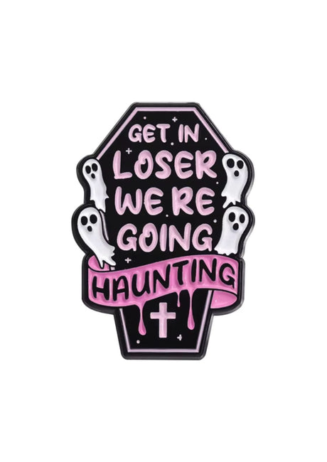 Ein schwarzer, sargförmiger Emaille-Anstecker mit pinker Schrift, die ‘steig ein, Verlierer, wir gehen spuken’ sagt, und weißen Geisterfiguren darum herum.