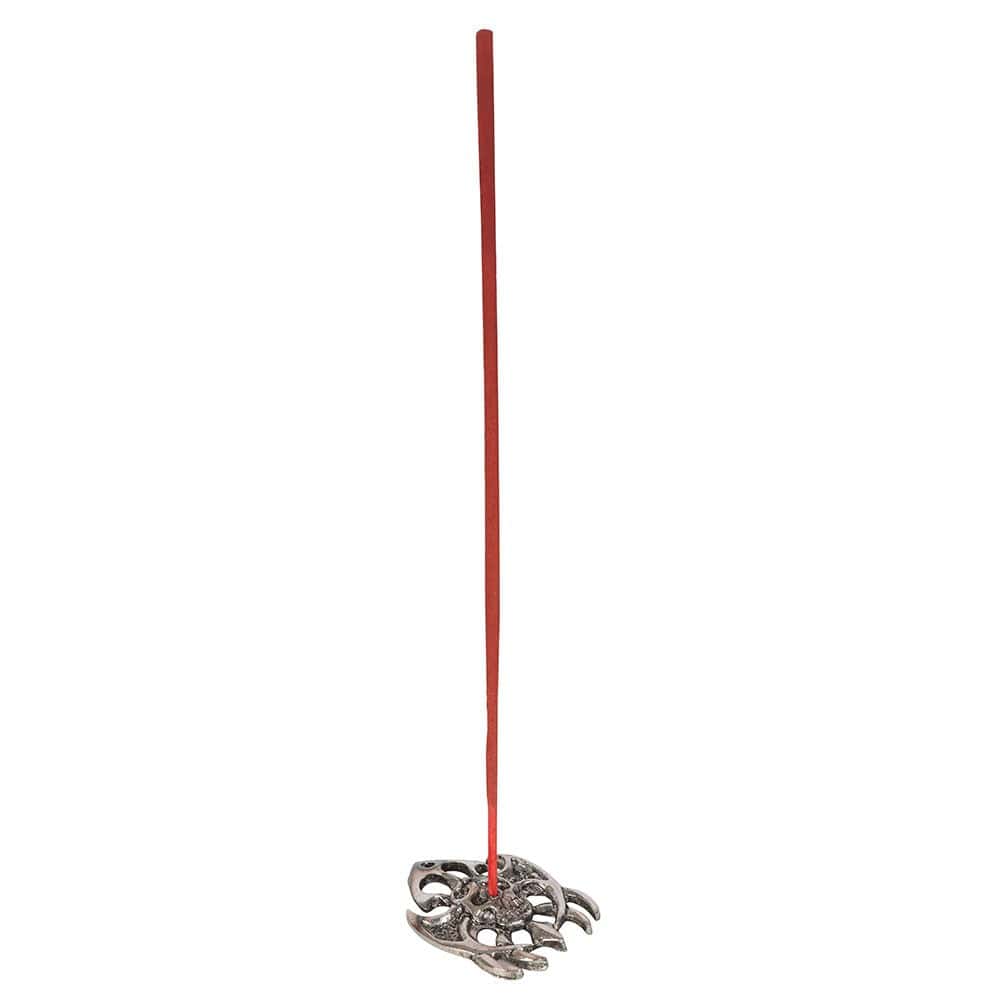 A slender red away evil incense stick stands upright in an ornate silver-toned metal holder with spider-like design