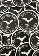 Schwarze runde Flecken mit weiß bestickten Fledermäusen, Swastikas in einem Mülleimer und dem Text ‚Goths gegen Faschismus‘ und ‚in unserem Schwarz gibt es kein Braun.‘
