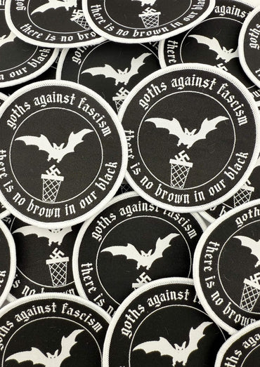 Schwarze runde Flecken mit weiß bestickten Fledermäusen, Swastikas in einem Mülleimer und dem Text ‚Goths gegen Faschismus‘ und ‚in unserem Schwarz gibt es kein Braun.‘