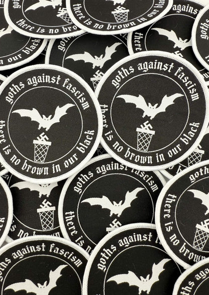 Schwarze runde Flecken mit weiß bestickten Fledermäusen, Swastikas in einem Mülleimer und dem Text ‚Goths gegen Faschismus‘ und ‚in unserem Schwarz gibt es kein Braun.‘
