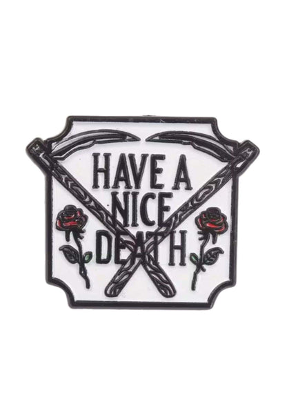 Weißer Emaille-Anstecker mit schwarzem Rand, gekreuzten Sensen und roten Rosen neben ’Have a nice death’ in fetter schwarzer Schrift