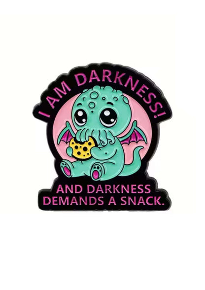 Eine niedliche Cthulhu-ähnliche Emaille-Anstecknadel mit dem Text ’I AM DARKNESS! UND DIE DUNKELHEIT VERLANGT EINEN SNACK’.