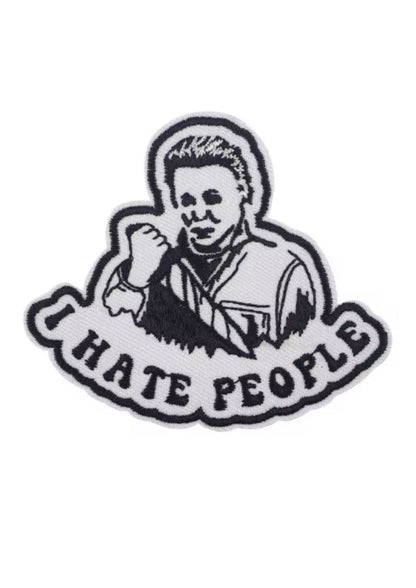 Weißer und schwarzer gestickter Aufnäher mit einer Person, die ein Messer hält, und dem Text ’I HATE PEOPLE’.
