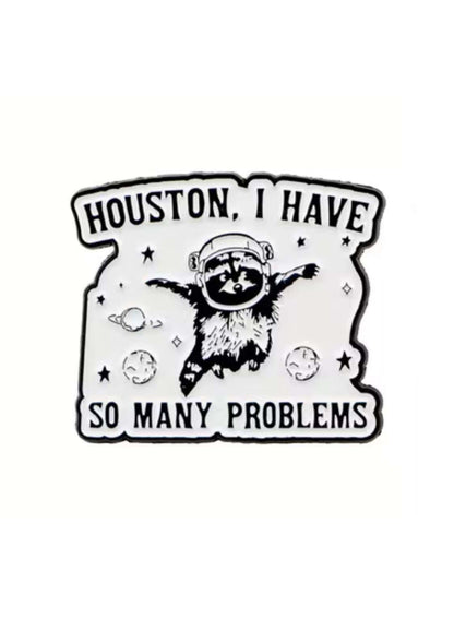 Weißer Emaille-Anstecker mit schwarzem Waschbär-Astronauten, umgeben von Sternen und Planeten, Text: Houston, ich habe so viele Probleme