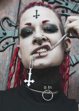 Gothic-Frau mit Piercings und umgekehrtem Kreuzschmuck.