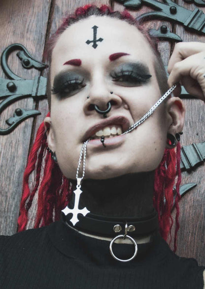 Gothic-Frau mit Piercings und umgekehrtem Kreuzschmuck.