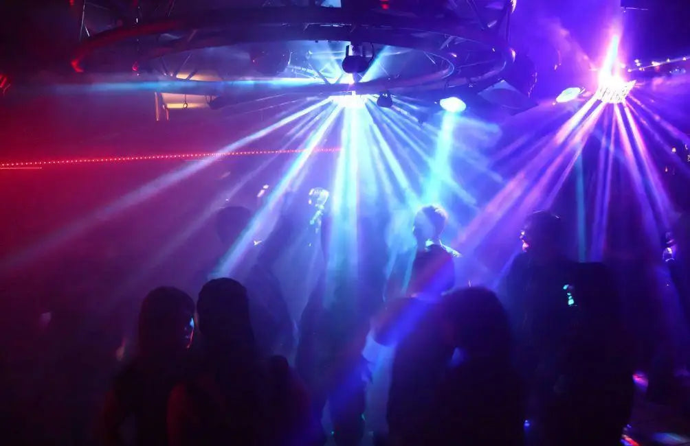 Leuchtende blaue und rote Laserlichter strahlen von einer Deckenkonstruktion in einen schwach beleuchteten Nachtclub hinab.