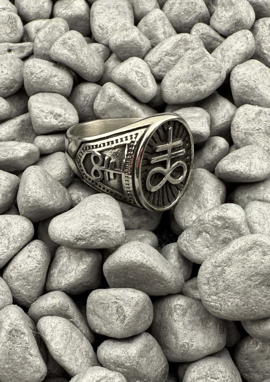 Leviathan ring aus edelstahl in silber mit eingraviertem sigil auf strukturiertem band auf grauen kieseln aus china
