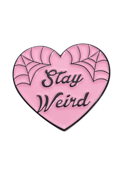 Rosa herzförmiger Email-Anstecker mit schwarzer Spinnennetz-Verzierung und dem Spruch ’stay weird’ in einer kursiven Schrift.
