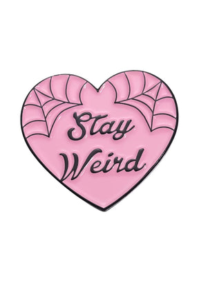 Rosa herzförmiger Email-Anstecker mit schwarzer Spinnennetz-Verzierung und dem Spruch ’stay weird’ in einer kursiven Schrift.