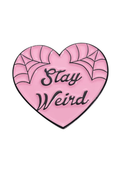 Rosa herzförmiger Email-Anstecker mit schwarzer Spinnennetz-Verzierung und dem Spruch ’stay weird’ in einer kursiven Schrift.