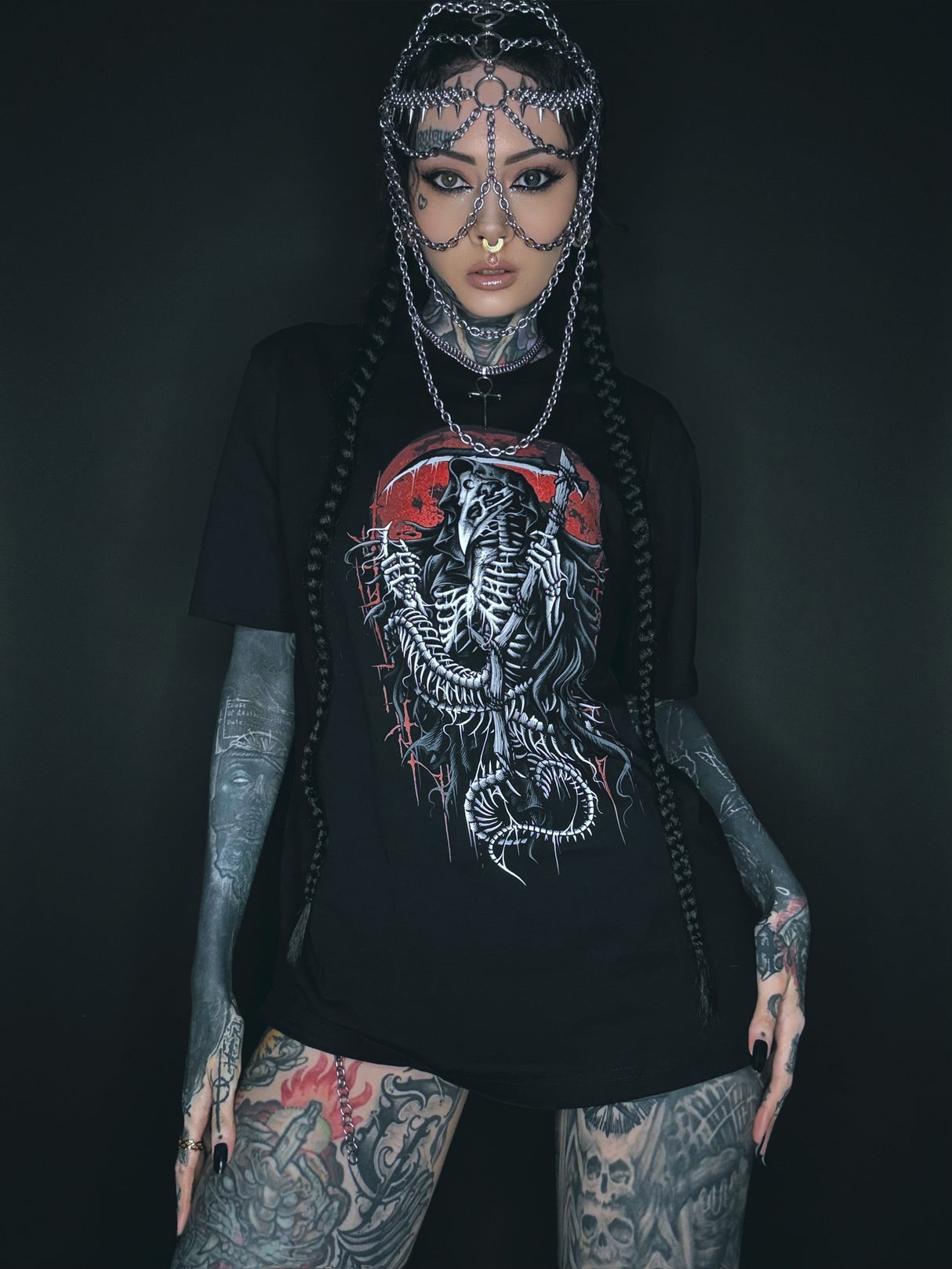 Tätowierte Frau, die einen Kettenkopfschmuck und ein grafisches T-Shirt trägt.