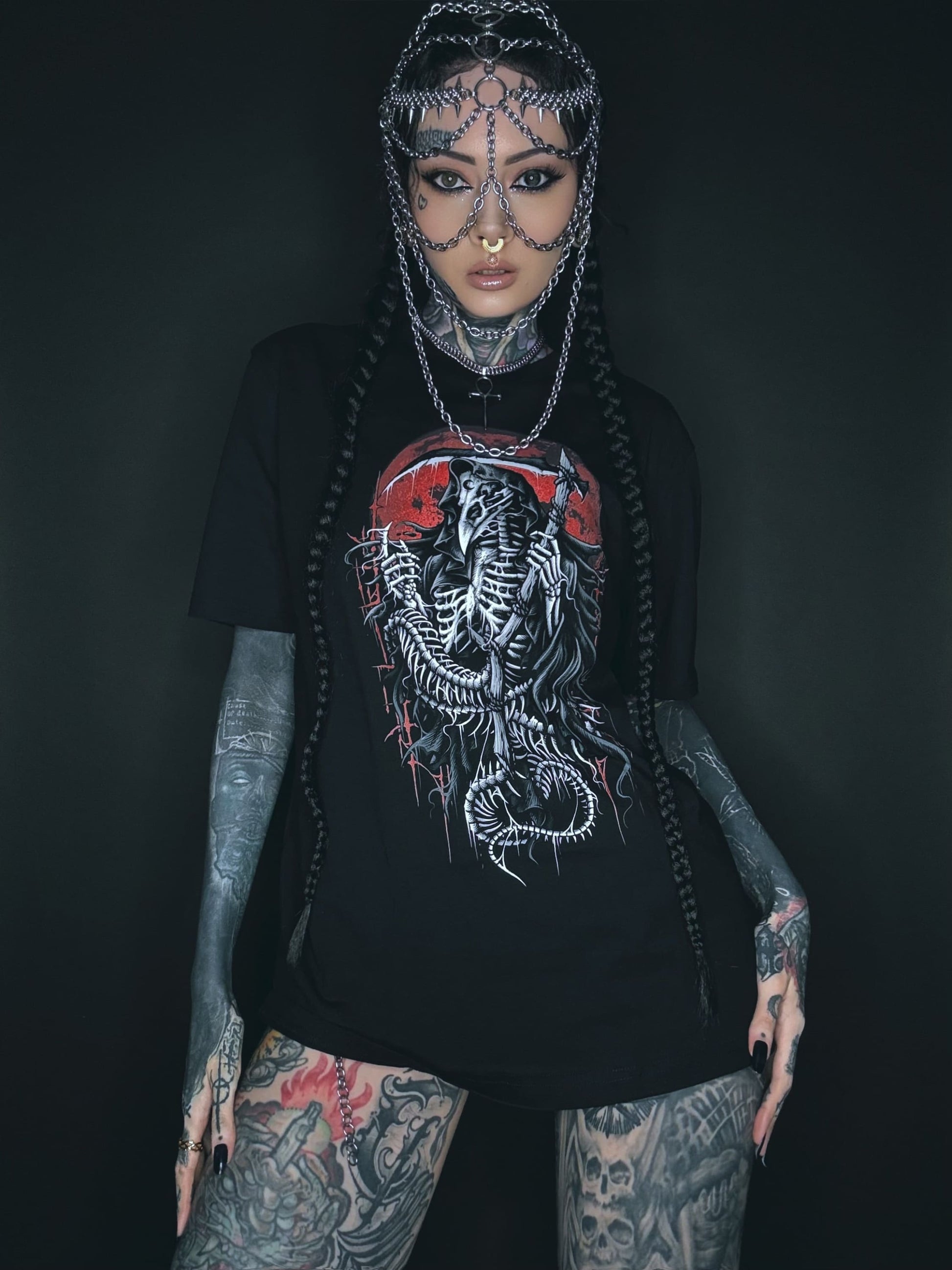 Tätowierte Frau, die einen Kettenkopfschmuck und ein grafisches T-Shirt trägt.