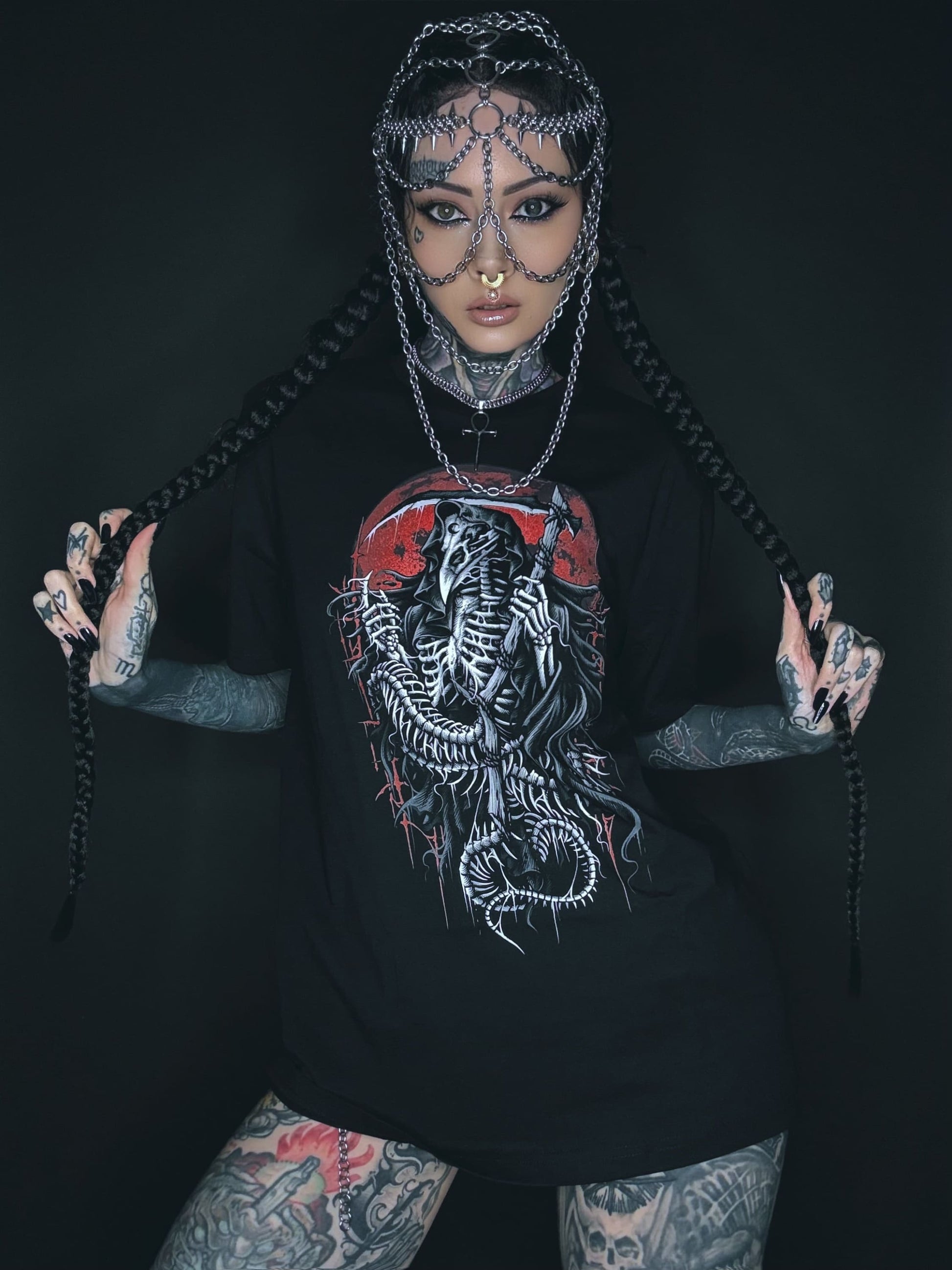 Tätowierte Frau mit Kettenkopfschmuck und grafischem T-Shirt.