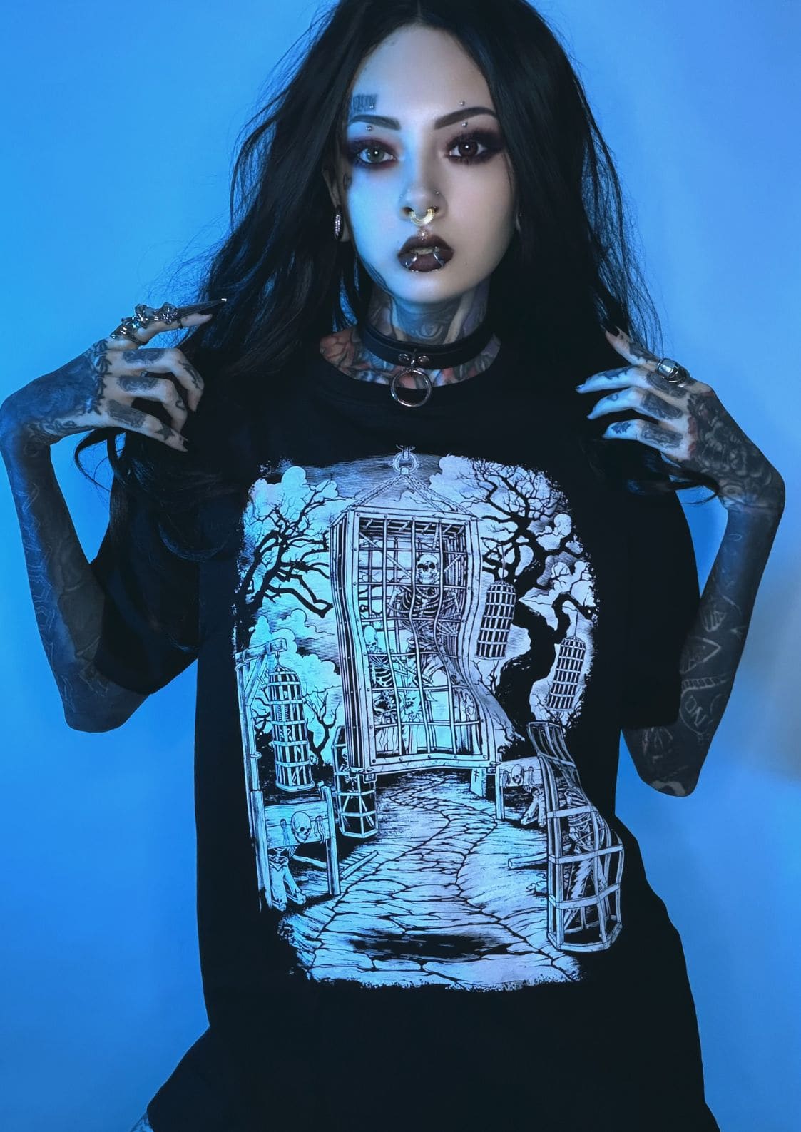 Schwarzes T-Shirt mit einem detaillierten weißen Grafikdruck, der eine gotische Szene mit Käfigen, Bäumen und skelettierten Figuren darstellt.