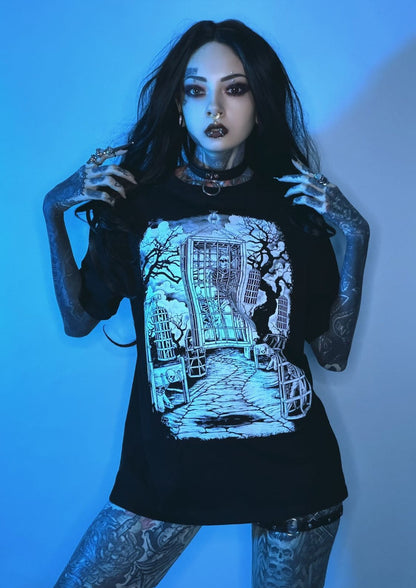 Schwarzes Grafik-T-Shirt mit einer weißen und hellblauen Illustration einer gotischen Szene, die ein Skelett in einem ornamentalen Tor zeigt, umgeben von Bäumen und Käfigen.