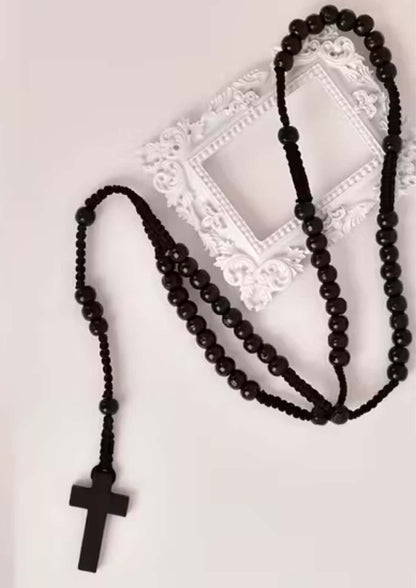 Schwarzes Perlenrosenkranz mit Holzkreuz-Anhänger, wahrscheinlich aus dunklem Holz oder Harz gefertigt.