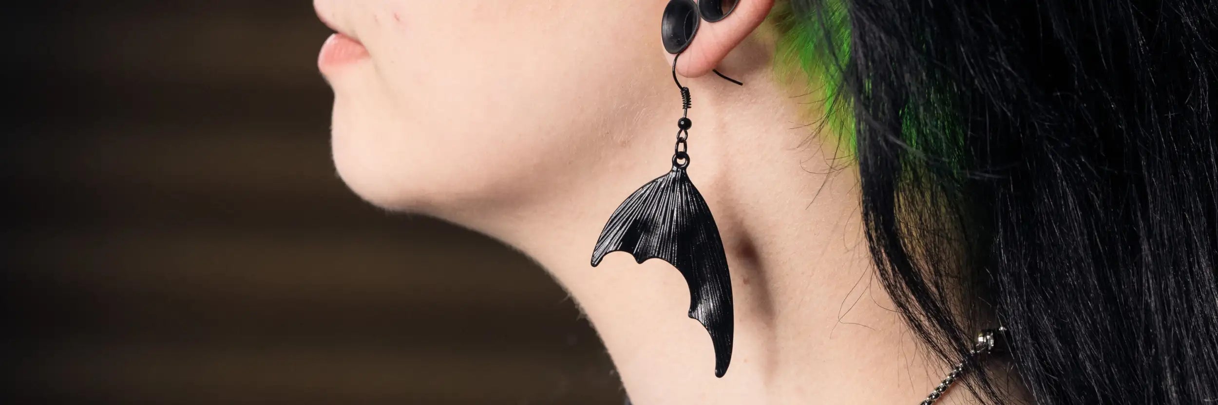 Schwarze, fledermausförmige Anhängerohrringe mit texturierter, metallischer Oberfläche.