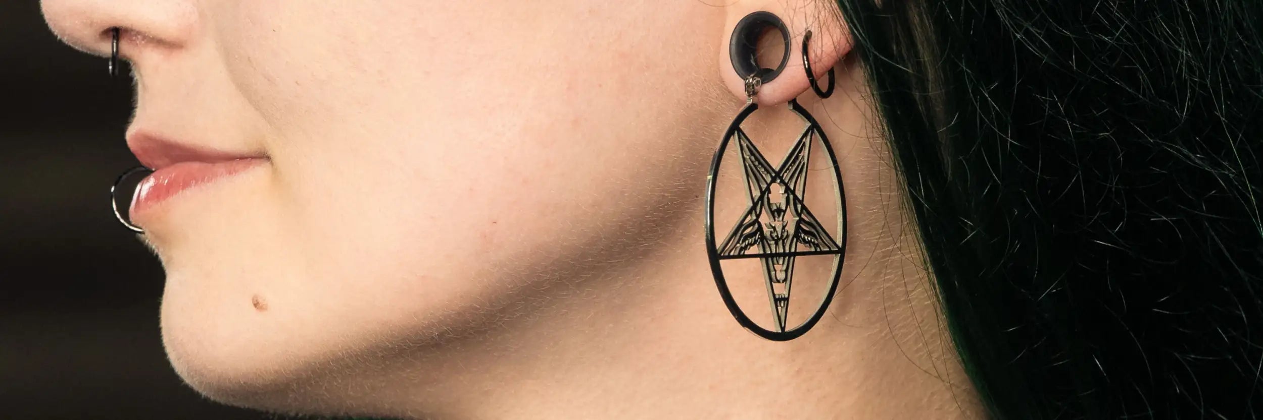 Schwarzes ovalförmiges Ohrring mit Pentagramm-Design, das ein umgekehrtes Dreieck und eine zentrale Figur zeigt, getragen durch ein gedehntes Ohrpiercing.