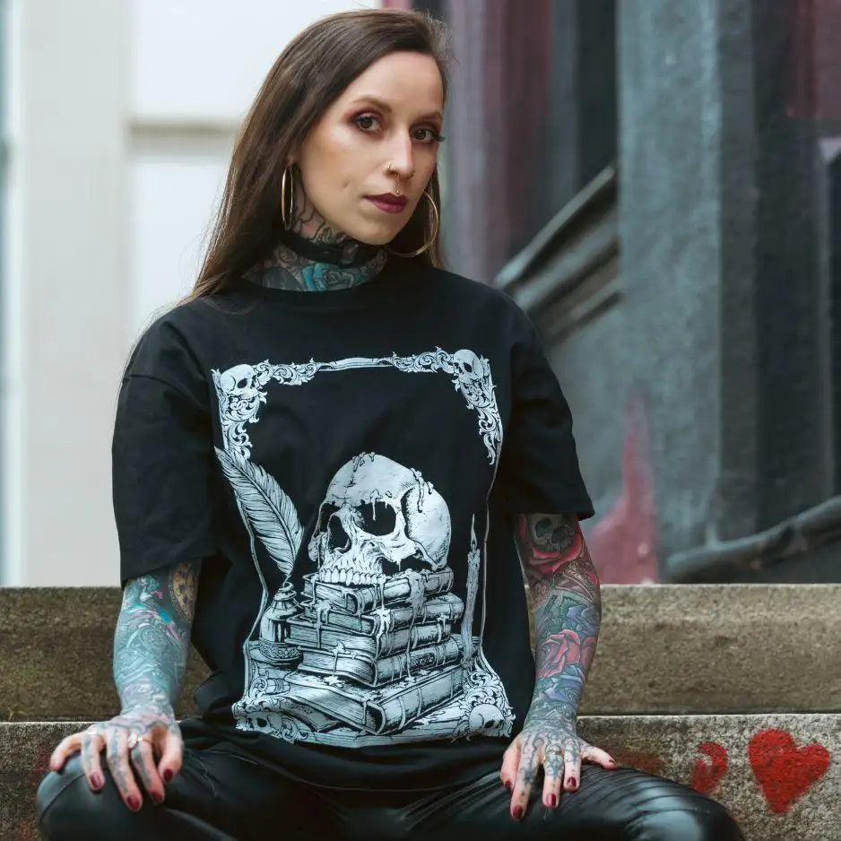 Schwarzes T-Shirt mit einem detaillierten weißen Grafikmotiv eines Schädels, der auf gestapelten Büchern ruht, umrahmt von ornamentaler Schriftzugarbeit und flankiert von Federn.