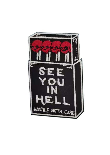 Black and white embroidered gothic patch shaped like a matchbox with red skulls and see you in hell text