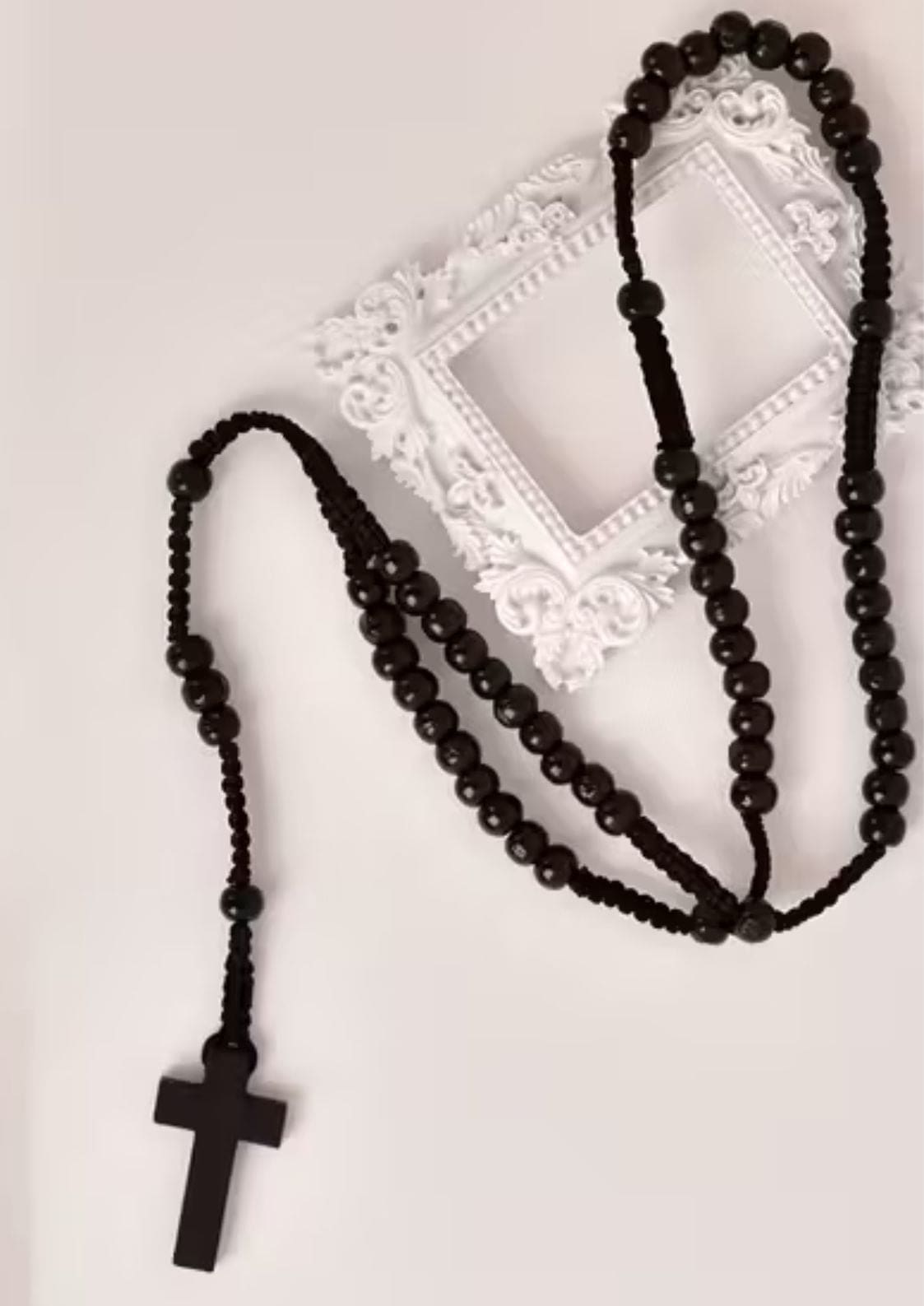 Schwarzes Perlenrosenkranz mit Holzkreuz-Anhänger, wahrscheinlich aus dunklem Holz oder Harz gefertigt.