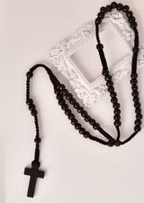 Schwarzes Perlenrosenkranz mit Holzkreuz-Anhänger, wahrscheinlich aus dunklem Holz oder Harz gefertigt.