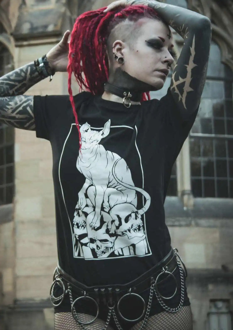 Tätowierte Frau mit roten Dreadlocks, die ein Katzen- und Totenkopf-T-Shirt trägt.