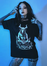 Schwarzes kurzärmliges T-Shirt mit detaillierter weißer Grafik einer gehörnten Figur, die auf einem Pentagramm mit Kerzen und einem Kreuz sitzt, gestaltet in einer okkulten Ästhetik.
